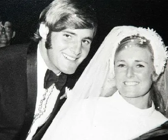 A black and white photo of a smiling couple on their wedding day; the bride wears a veil, and the groom is in a suit.