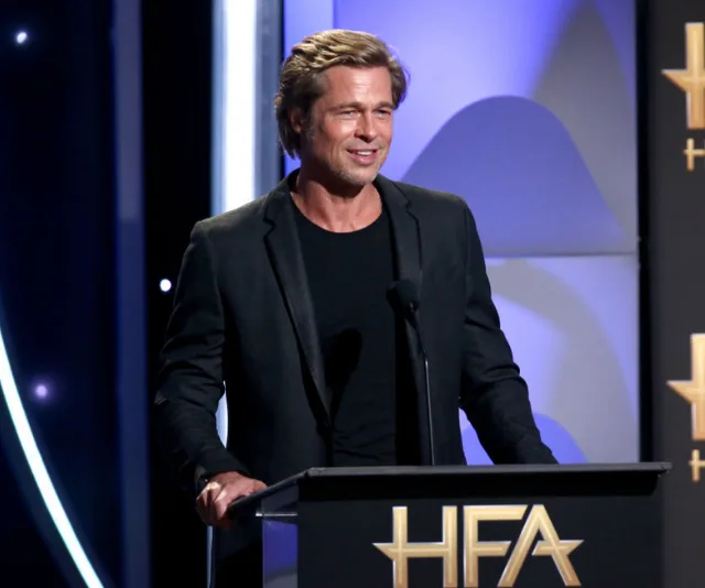 Actor in a suit, standing at a podium with "HFA" logo, speaking at an awards event.