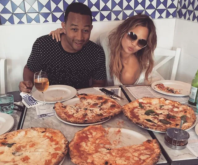 Two people enjoying a meal with several pizzas on a table in a restaurant setting.