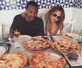 Two people enjoying a meal with several pizzas on a table in a restaurant setting.