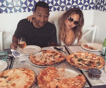Two people enjoying a meal with several pizzas on a table in a restaurant setting.