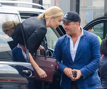 A couple smiling and talking beside a car, with one holding a maroon handbag.