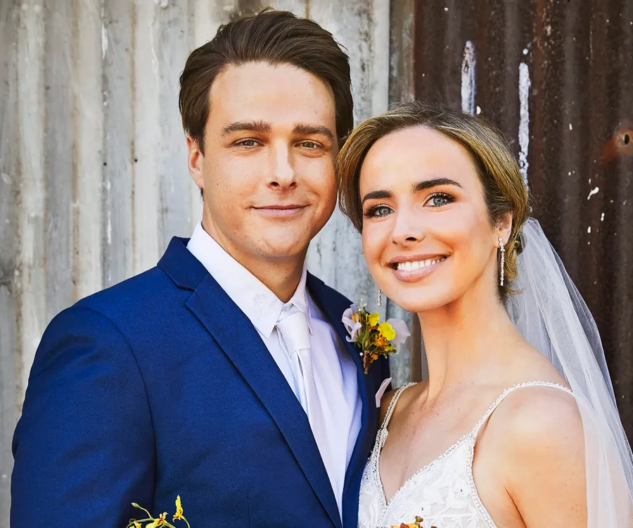 A bride and groom smiling on their wedding day, with the groom in a blue suit and the bride in a white dress and veil.