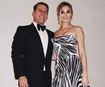 A couple posing together, man in a tuxedo and woman in a black and white patterned strapless dress.