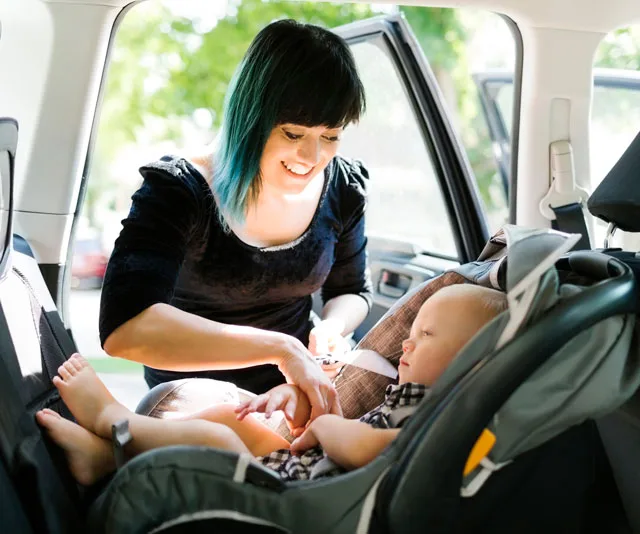 Mother securing baby in forward-facing car seat inside a vehicle.