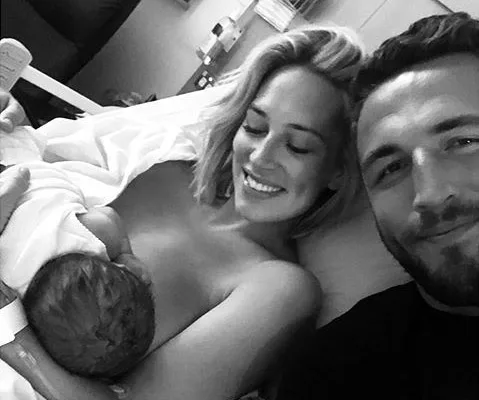 A couple smiling with their newborn baby in a hospital bed.