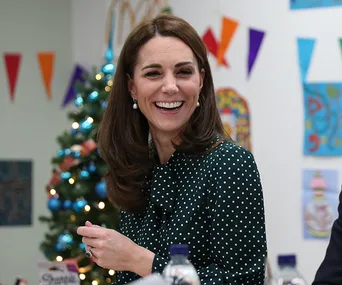 Smiling woman in green polka dot dress, sitting in a decorated room with a Christmas tree and colorful bunting.