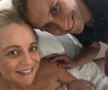 Family in hospital bed with newborn baby, all smiling.