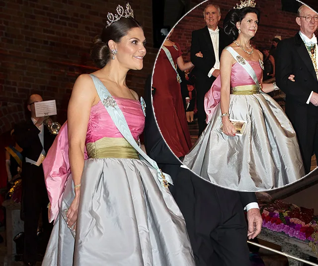 Two women in elegant gowns with sashes and tiaras at a formal event.