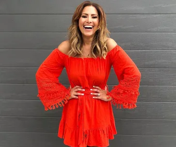Smiling woman in a bright red, off-the-shoulder dress with bell sleeves stands against a gray background.