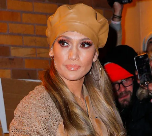Woman in brown beret and hoop earrings, outdoors, with people in background.