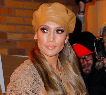 Woman in brown beret and hoop earrings, outdoors, with people in background.