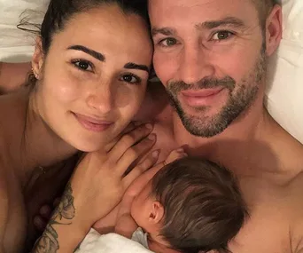 A couple smiling while lying in bed with a baby nestled between them.