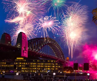Fireworks illuminate the Sydney Harbour Bridge at night, with vibrant colors lighting up the sky.