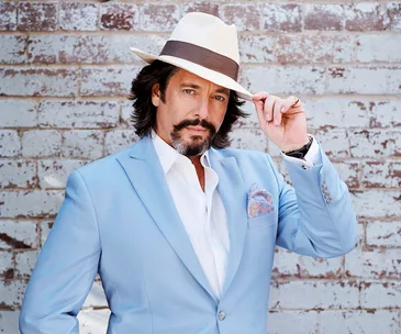 Man in a light blue suit and hat poses confidently against a brick wall.