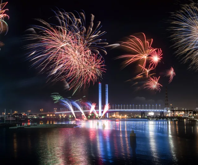 Melbourne New Year's Eve fireworks illuminate the night sky over a river, reflecting vibrant colors on the water.