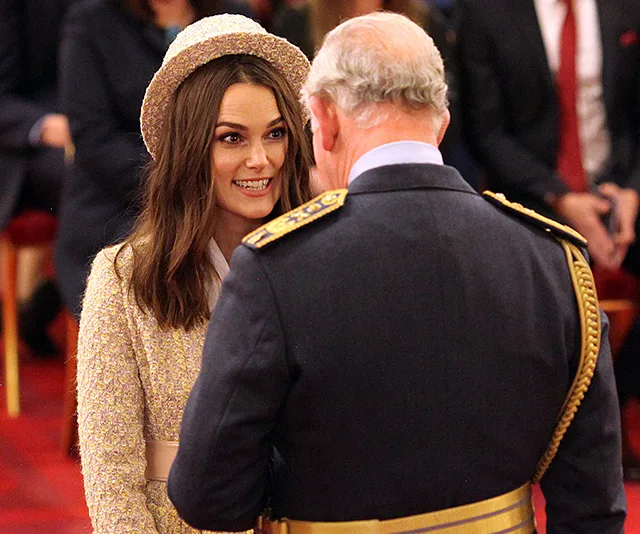 A woman in formal attire smiles while speaking to an older man in a military uniform, in a ceremonial setting.