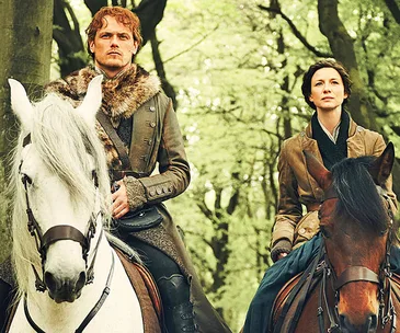 Sam Heughan and Caitriona Balfe as characters on horseback in a forest scene from "Outlander".