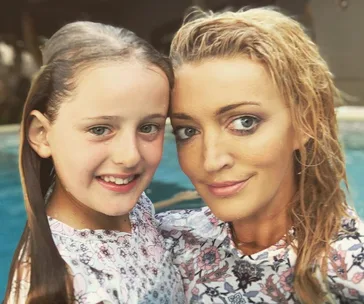 A woman and a young girl smiling together in front of a pool, both wearing floral-patterned outfits.