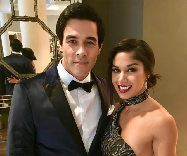 Man in a tuxedo and woman in an elegant dress smiling at a formal event.