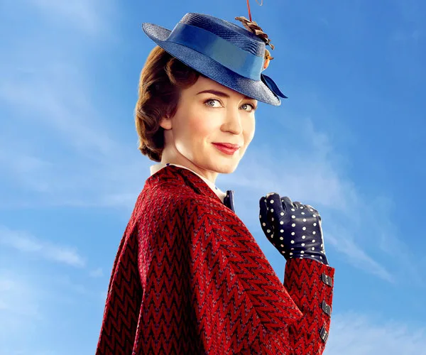 Emily Blunt as Mary Poppins in a vibrant red coat and blue hat against a clear sky in "Mary Poppins Returns."