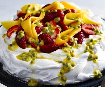 Pavlova topped with strawberries, mango slices, and passion fruit.