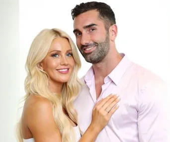 A smiling couple posing together, the woman with blonde hair and the man in a light shirt, both seeming happy.