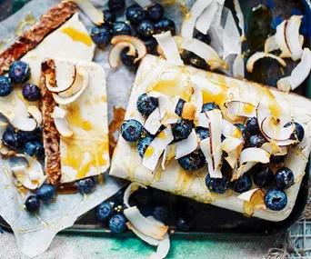 Frozen parfait topped with blueberries, coconut flakes, and drizzled with honey on parchment paper.