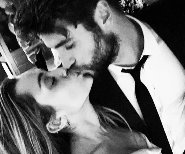 A couple sharing a kiss, dressed formally, celebrating an intimate moment possibly at a wedding.
