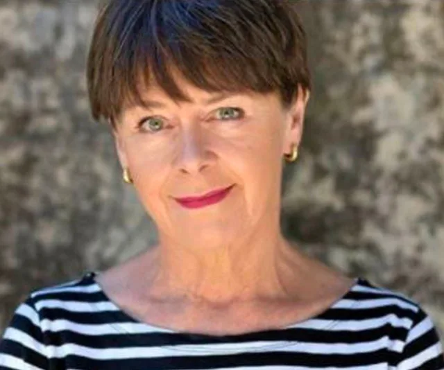 Woman with short brown hair, wearing a striped shirt, smiles at the camera against a blurred background.