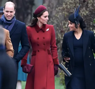 A man and two women in elegant winter outfits, walking outside and smiling, with trees in the background.
