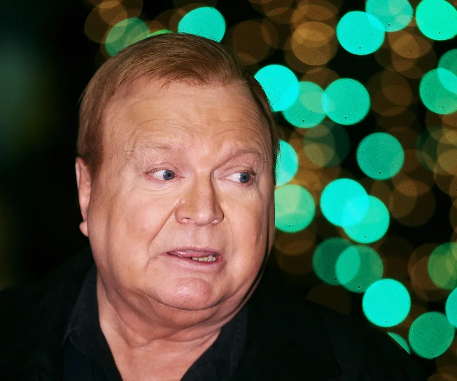 A person with light hair looking to the side against a blurred backdrop of circular green lights.