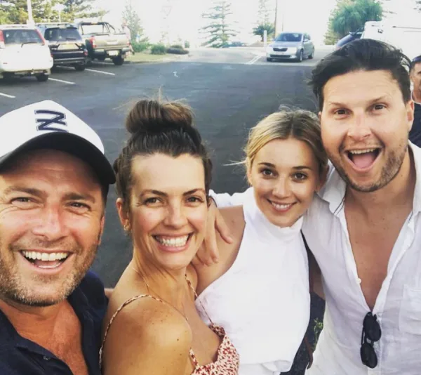 Group selfie of two men and two women smiling in an outdoor parking area.