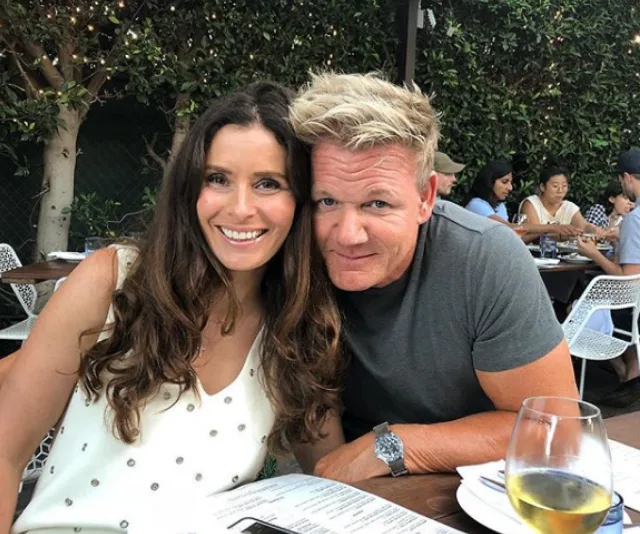 Couple smiling while seated outdoors at a restaurant, with trees and other diners in the background.