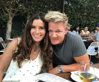 Couple smiling while seated outdoors at a restaurant, with trees and other diners in the background.