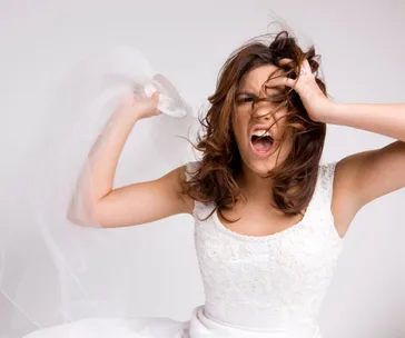 Angry bride in a white dress pulling her hair and yelling.