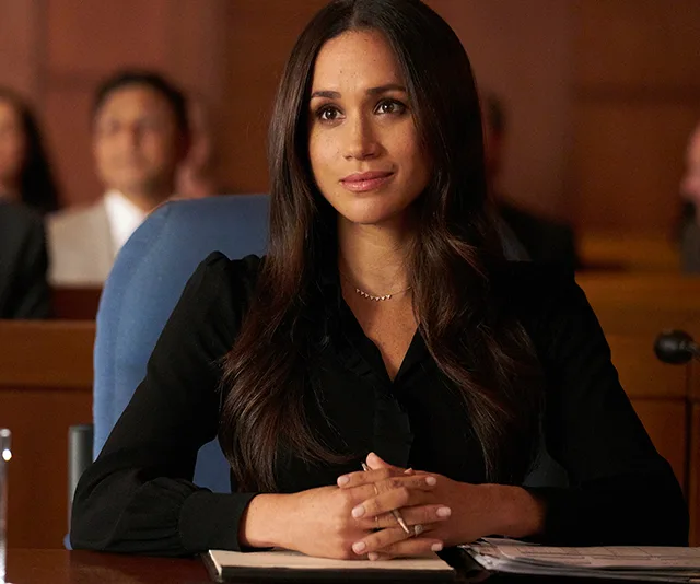 "Person sitting in a courtroom, hands clasped on desk, wearing a black shirt."