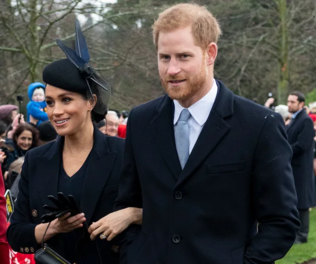Couple dressed formally, outdoors, surrounded by people and trees in the background.