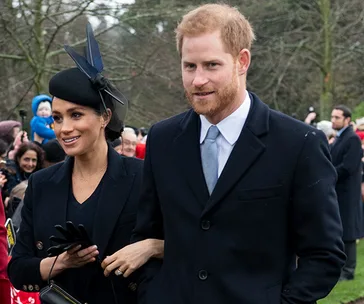 Couple dressed formally, outdoors, surrounded by people and trees in the background.