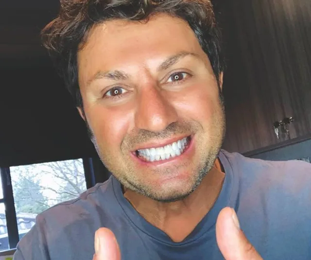 Smiling man giving thumbs up indoors with kitchen background.