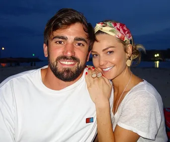 Couple smiling on a beach at dusk, with the woman wearing a headscarf and the man in a white t-shirt.