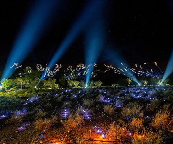 Desert landscape illuminated by vibrant blue lights and patterns under a night sky at the Parrtjima Light Festival.