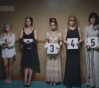 Women from "Big Little Lies" in evening attire, holding numbered signs, standing in a lineup against a wall.