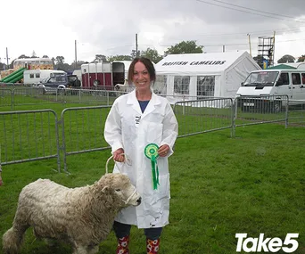 A woman in a white coat poses with a cow and a ribbon at an agricultural fair.