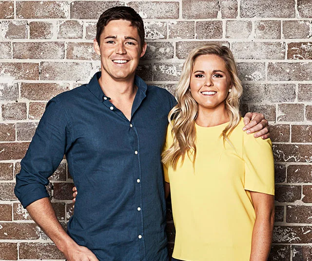 Two people smiling and standing in front of a brick wall, one in a blue shirt and the other in a yellow top.