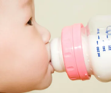 A baby drinking milk from a bottle with a pink cap, close-up side view.