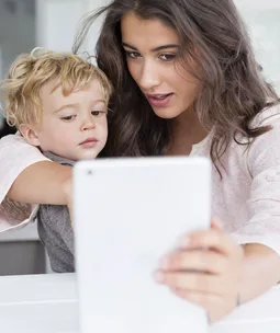 "A woman and a toddler looking at a tablet screen together."