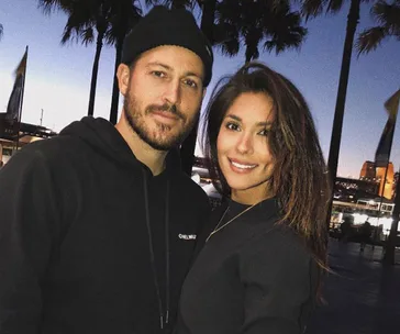 Couple smiling with cityscape and palm trees in the background at dusk.