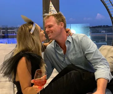 A couple smiling at each other, wearing party hats, with a sunset view in the background.