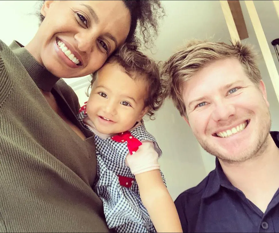 A happy couple poses with their smiley toddler, capturing a joyful family moment indoors.